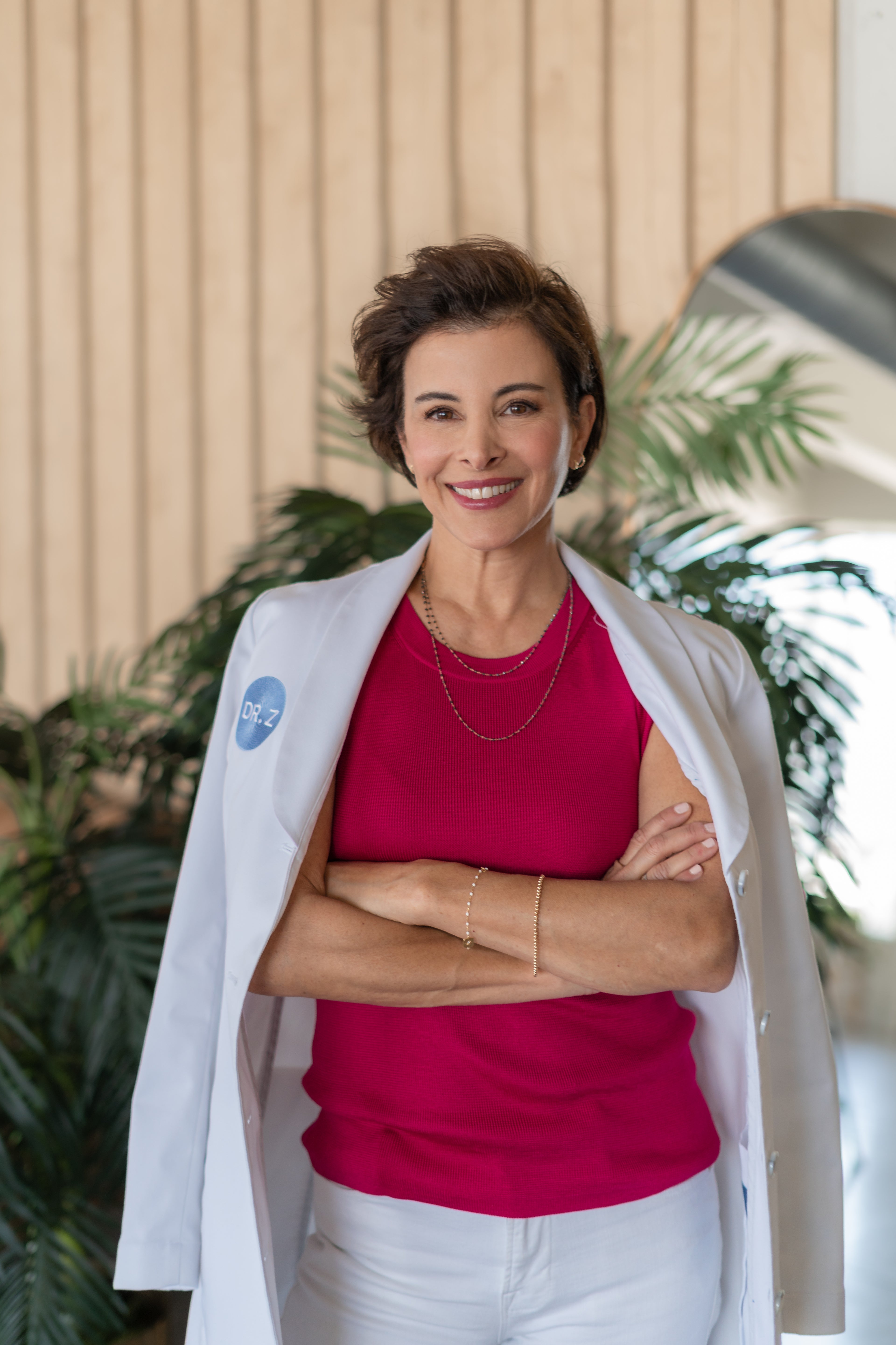 Dr.Zenovia wearing a white lab coat over a pink shirt with plants in the background