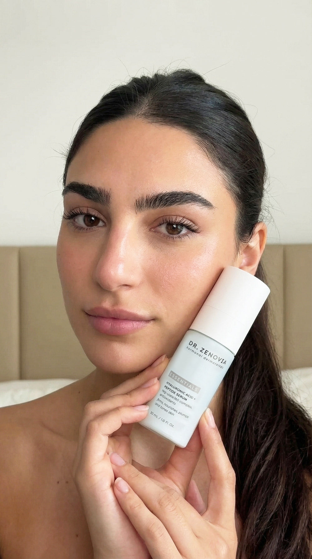 Woman holding a skincare product with a neutral background