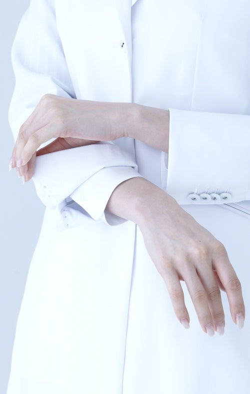 Close-up of a person wearing a white coat with hands resting on the lap.