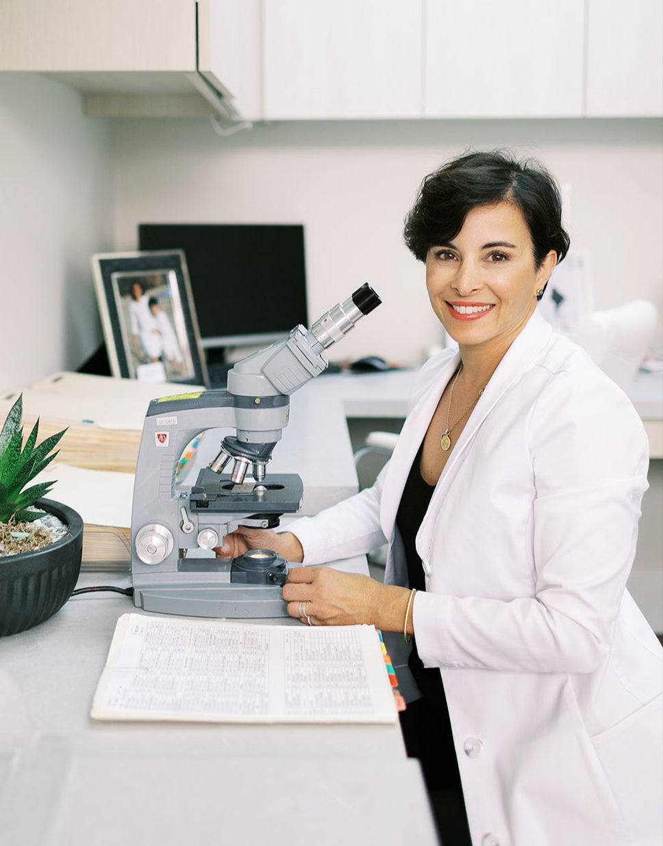 Dr. Zenovia in a lab coat using a microscope in a laboratory setting