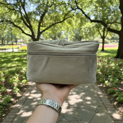 Beige fabric pouch held in front of a park with green trees and flowers.
