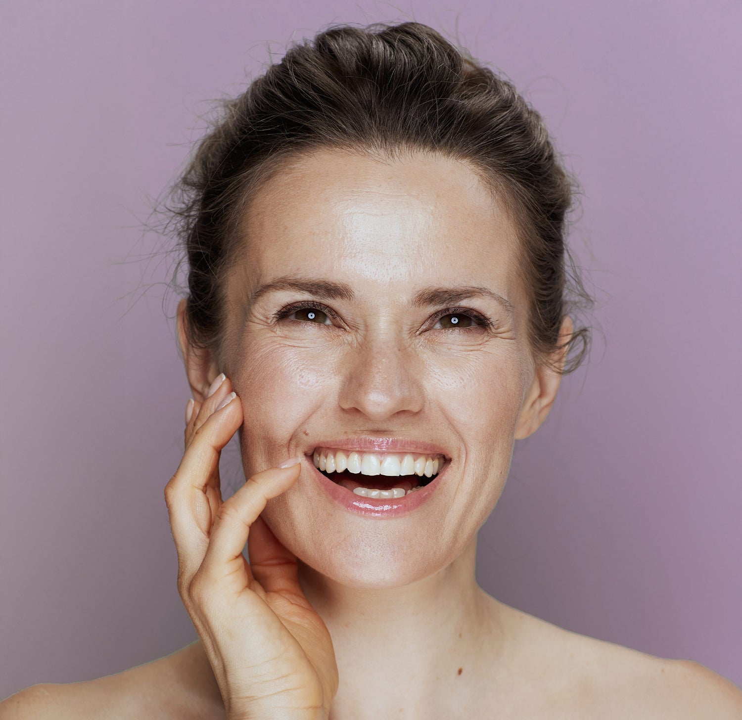 Woman smiling with hand on face against a purple background
