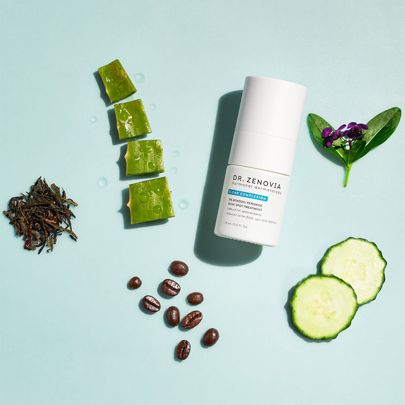 Benzoyl Peroxide Spot Treatment bottle with aloe, coffee beans, cucumber slices, and green leaves on a light blue background